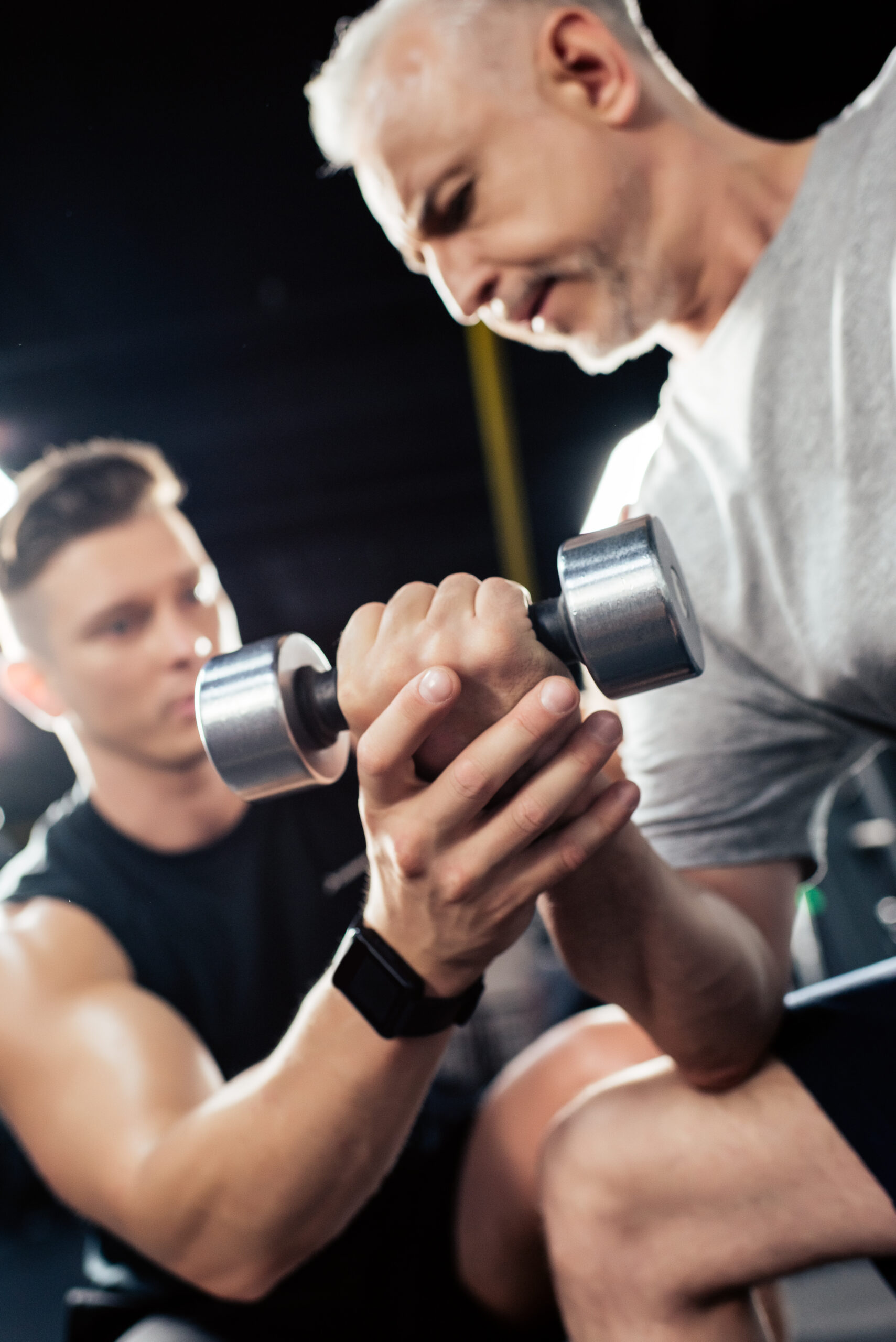 senior sportsman training with dumbbell and young trainer in sport center